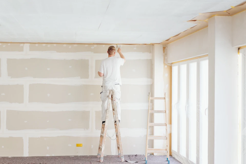 Un artisan mesure et marque une planche de bois avec une &eacute;querre m&eacute;tallique et un crayon lors de travaux de construction ext&eacute;rieure